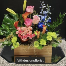 Mixed floral arrangement with roses, calla lilies, and blue delphinium in a wooden box
