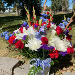 Bouquet of red roses, white lilies, and blue flowers in a white vase with a striped ribbon.