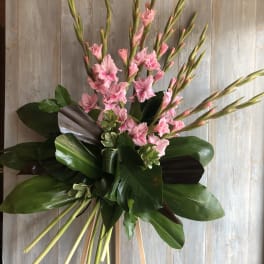 Tall arrangement of pink flowers with large glossy leaves on a wooden stand