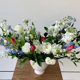 White and blue floral arrangement with pink tulips in a white vase