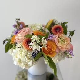 Mixed bouquet of peach, orange, white, and purple flowers in a white vase