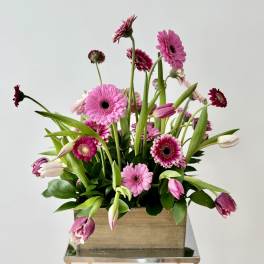 Pink gerbera daisies and tulips arranged in a wooden box