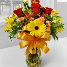 Bouquet of red and yellow flowers in a glass vase with a gold ribbon