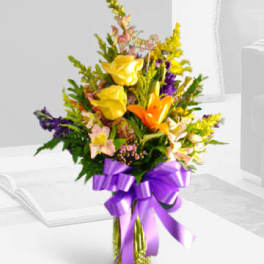 Tall bouquet of yellow roses, orange lilies, and purple flowers tied with a purple ribbon