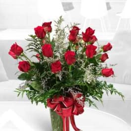 Red roses arranged in a glass vase with a red ribbon