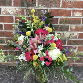 Mixed bouquet in a glass vase with pink lilies, gerbera daisies, roses, and white blooms