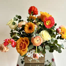 Mixed bouquet of orange, pink, red, and white flowers in a wooden box