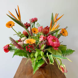 Tropical bouquet with pink peonies, orange gerbera daisies, and bird of paradise in a vase