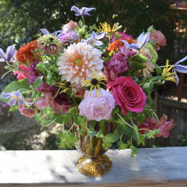 Mixed bouquet of pink, peach, and purple flowers in an amber vase