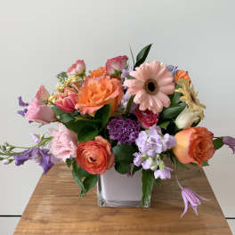 Mixed bouquet in a square glass vase with pink, orange, and purple flowers