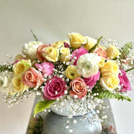 Mixed roses in pink, yellow, peach, and white arranged in a white vase