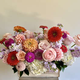 Low mixed flower arrangement in a rectangular wooden box with pink, red, and lavender blooms.