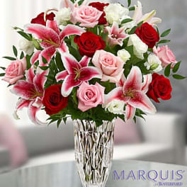 Tall bouquet of pink lilies, red and pink roses, and white blooms in a cut crystal vase