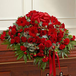 Red rose, gerbera daisy, and carnation casket spray with ribbons on a wooden casket