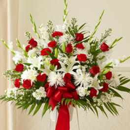 Tall red and white standing floral arrangement with roses, lilies, and bow on an easel