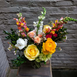 Mixed bouquet of roses, ranunculus, and snapdragons in a glass vase
