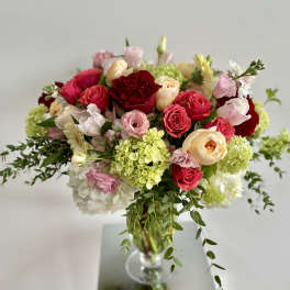 Mixed arrangement of red, pink, and peach roses with green hydrangeas in a clear glass vase