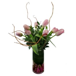 Pink tulips arranged in a tall glass vase with curly branches