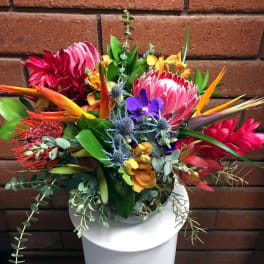 Vibrant tropical arrangement with protea, orchids, and birds of paradise in a glass vase on a white stand