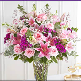 Tall arrangement of pink roses and lilies with bright fuchsia blooms in a clear glass vase