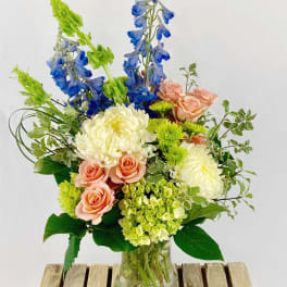 Mixed bouquet in a glass vase with blue delphinium, peach roses, and white chrysanthemums