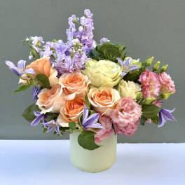 Pastel bouquet of roses, lisianthus, and purple blooms in a pale vase