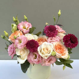 Pink and peach roses with magenta blooms in a white vase