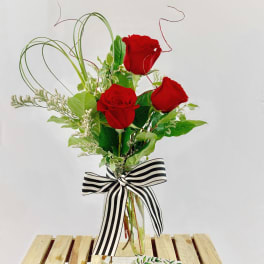 Three red roses in a clear glass vase with a striped bow