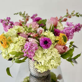Mixed bouquet of pink, yellow, and green flowers in a textured vase
