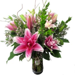 Pink lilies in a glass vase with mixed greenery