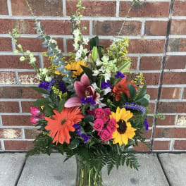 Colorful mixed bouquet in a clear glass vase with lilies, gerberas, roses, and sunflowers