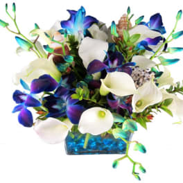 Bouquet of white calla lilies and blue-purple orchids in a blue glass vase