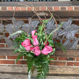 Pink roses arranged in a glass vase with branches and greenery