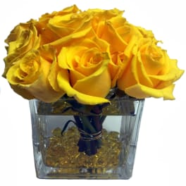 Yellow roses arranged in a clear square vase with decorative stones