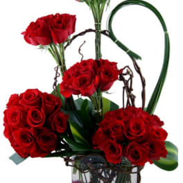 Red rose arrangement in a clear glass vase with decorative loops