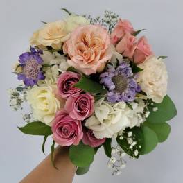 Handheld bouquet of pink, peach, white, and purple roses with small filler flowers