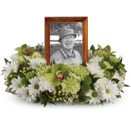 Low wreath of white and green flowers forming a ring around a wooden frame with a black-and-white portrait.