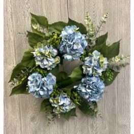Round wreath of blue hydrangea blooms with green foliage on a wood background