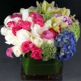Mixed bouquet of roses, calla lilies, orchids, and hydrangea in a glass vase