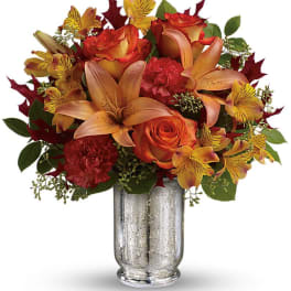 Orange roses and lilies arranged in a silver vase