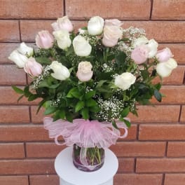 Pink and white roses in a glass vase with a pink ribbon bow