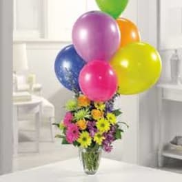 Colorful balloon bouquet above a mixed flower arrangement in a glass vase