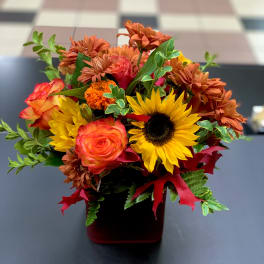 Bouquet of sunflowers, orange roses, and mums in a red vase