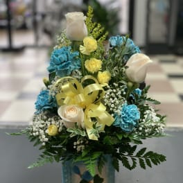 Blue and white floral arrangement in a decorative vase with a yellow ribbon