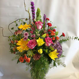 Colorful mixed bouquet in a clear glass vase with roses, lilies, and gerbera daisies