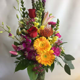Tall mixed bouquet in a clear glass vase with red roses and bright blooms