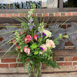 Mixed bouquet in a clear glass vase with pink, purple, and green flowers