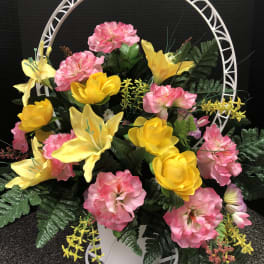 Pink and yellow floral arrangement in a white basket with a circular frame