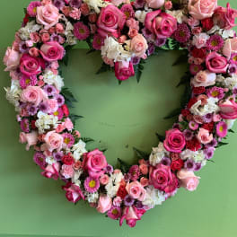 Heart-shaped floral wreath of pink and white roses on a green wall