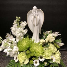 White floral arrangement with a praying angel statue in the center